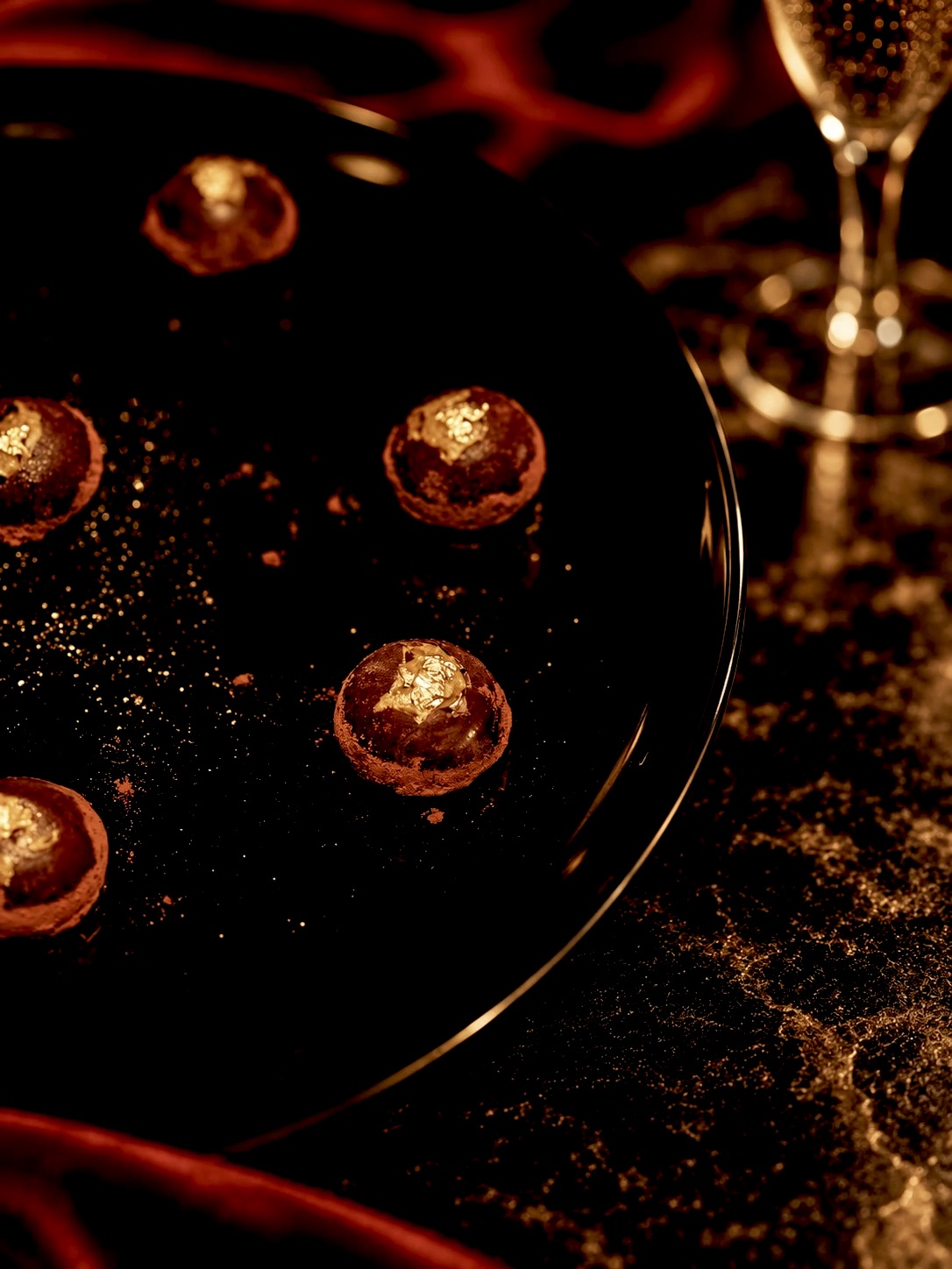 Gold-leaf truffles on a black plate beside champagne