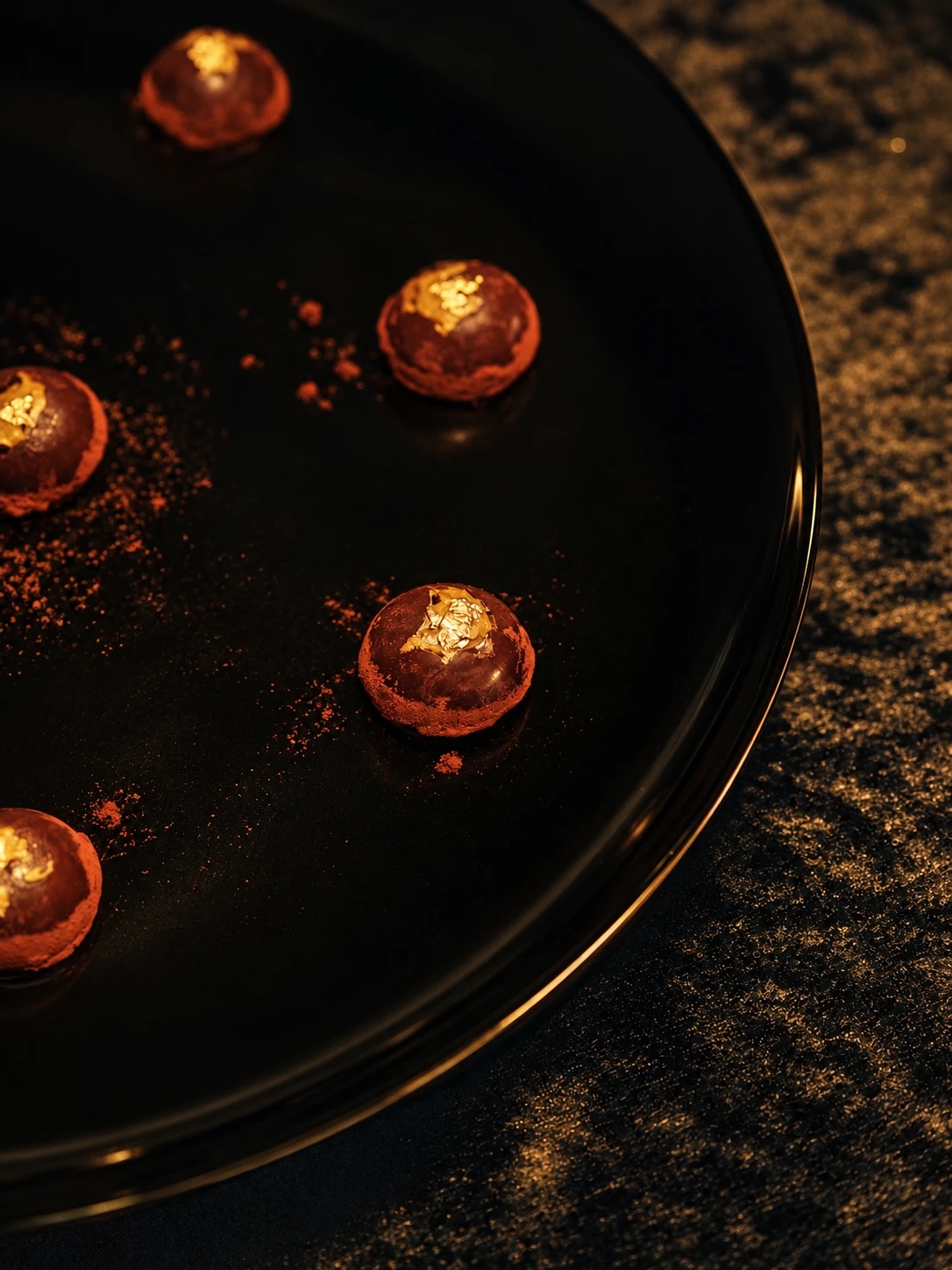 Elucium truffles crowned with gold leaf on a black plate